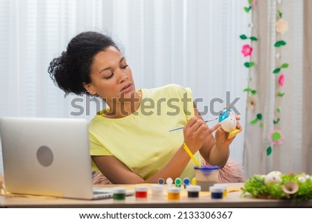 Cute African American woman talking by video call on a laptop. A young woman teaches a video lesson on painting Easter eggs, sitting at a decorated holiday table. Happy easter. Close up.