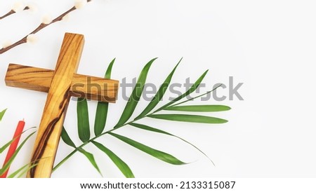 Easter religion composition with wooden crucifixion, palm leaf, willow branch and red church candle on a white background with copy space. The concept of Holy Week, Palm Sunday and Lent Royalty-Free Stock Photo #2133315087