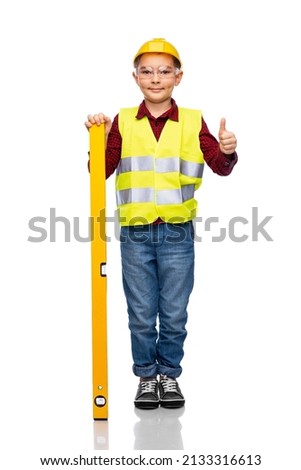building, construction and profession concept - little boy in protective helmet and safety vest with level showing thumbs up over white background