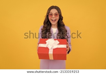 trendy amazed kid in sunglasses and suit hold present box on yellow background, present