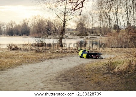 An old bicyclist fell with the bike and he is lying on the ground in nature.