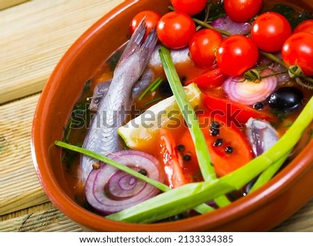 Fisher soup from whiting with tomatoes, red onion, bell pepper served with lemon, scallions and black olives in clay bowl