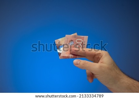 Paper banknote of 50 Canadian dollar bill held between fingers by Caucasian male hand. Close up studio shot, isolated on blue background.