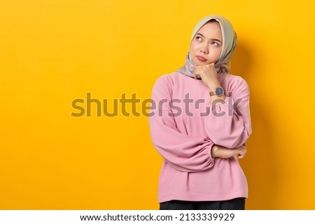 Pensive young Asian woman in pink shirt looks seriously thinking about a question on yellow background