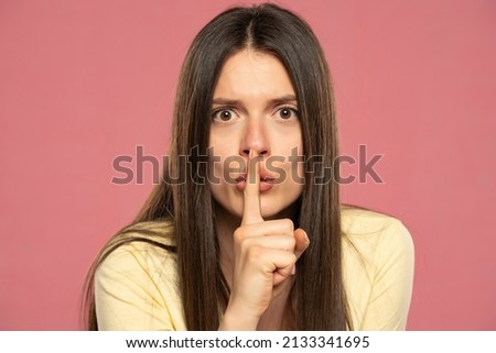 Portrait of young woman finger covering lips mouth do not tell look camera isolated on pink color background