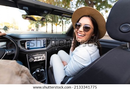 Joyful young woman sitting on convertible car smiling at camera - Happy couple driving on the road with cabriolet car - People on roadtrip enjoying freedom - Transportation concept Royalty-Free Stock Photo #2133341775