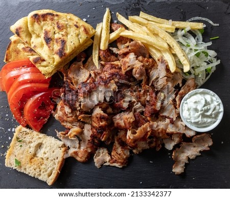 Greek gyro traditional meat food, Ethnic dish, meat cut into thin slice, pita bread and tzatziki yogurt on black color background, top view.