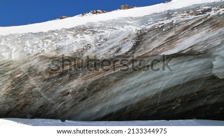 A huge ice wave froze in the mountains. View of the marble glacier. White snow, trails from people are visible. Tourists go to places and take photos. The ice has an unusual shape. Kazakhstan, Almaty