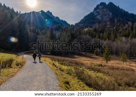 Two women walk on a winding dirt road between fields and mountains in late autumn on a sunny day in the Schwarzee region of Canton Fribourg, Switzerland. High quality photo