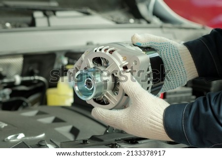Spare parts. A generator for an automobile engine on the car mechanic's desktop. Close-up. A mechanic inspects a new generator when replacing a faulty generator. Royalty-Free Stock Photo #2133378917