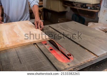 Trimming a piece of plywood intro exact measurements with a cabinet table saw, also known as tilting arbor saw. At a furniture making factory. Royalty-Free Stock Photo #2133382261