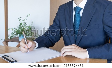 Men in suits. He writes on paper.