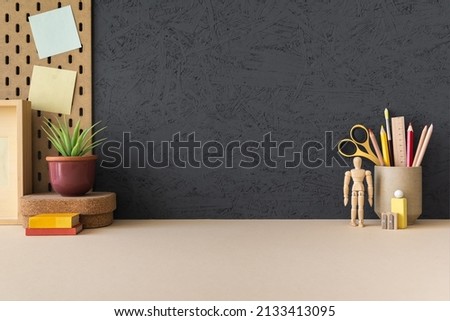 Creative desk with a blank picture frame or poster, desk objects, office supplies, books, and plant on a black background.