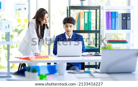 Asian young professional successful female businesswoman manager in white formal suit standing helping mentoring new recruitment businessman sitting working with laptop computer in company office.