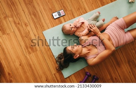High angle view of a mom lying on an exercise mat with her baby. Mother and baby taking a break from working out. New mom bonding with her baby during her post-natal fitness routine.
