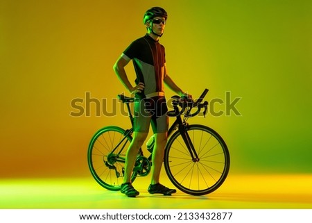 Cyclist riding a bicycle isolated on studio background in gradient yellow green neon light. Concept of active life, rest, travel, energy, sport