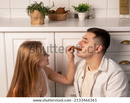 Happy young couple sitting on kitchen floor. Beautiful woman feeding husband or boyfriend. Romantic atmosphere in relationship concept. High quality photo