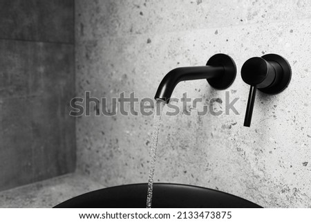 Picture of bathroom details: black washbasin and mounted tap with flowing water.