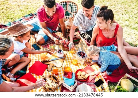 Multiracial families having fun together with kids at park on pic nic party - Genuine joy and love life style concept with mixed age people toasting juices with children at park - Warm bright filter