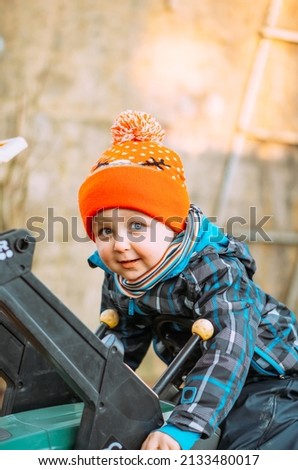 a little boy dressed in warm clothes plays with a toy tractor on the street