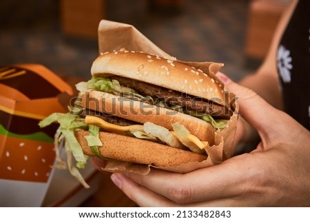 Burger in hand. Big tasty burger in the girl's hand.  Royalty-Free Stock Photo #2133482843