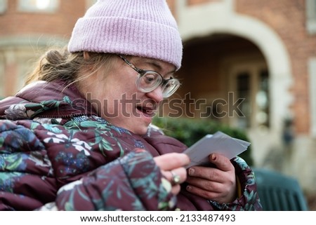 Outdoor portrait of a 39 year old white woman with the Down Syndrome looking at printed pictures