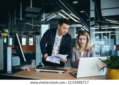 Two employees in a modern office, an Asian man and a woman working at a table, colleagues discussing and consulting, thinking about a joint project Royalty-Free Stock Photo #2133488717