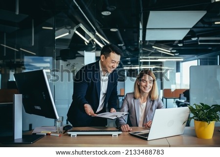Two employees in a modern office, an Asian man and a woman working at a table, colleagues discussing and consulting, thinking about a joint project Royalty-Free Stock Photo #2133488783