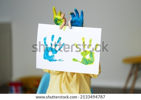 A sad child girl shows her hands painted in the colors of the Ukrainian flag, yellow and blue. Little Ukrainian patriot. Stop the war in Ukraine. 