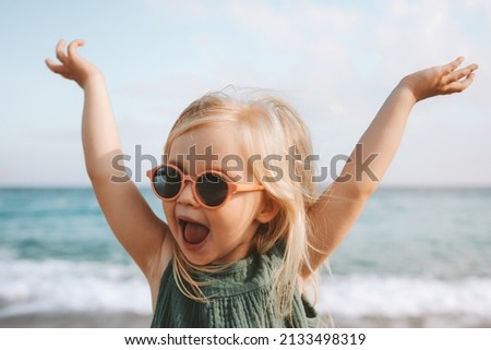 Funny kid girl playing outdoor surprised emotional child in sunglasses 3 years old baby raised hands family vacations  Royalty-Free Stock Photo #2133498319