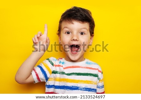 idea. child, boy emotionally points up. A gesture of an idea. Portrait of a child in a bright striped T-shirt on a yellow background, studio Royalty-Free Stock Photo #2133524697