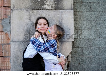 Portrait of two little girls embracing and kissing with Russian and Ukrainian flags on the faces. Concept of peace, stop the war and friendship of children against hate people
