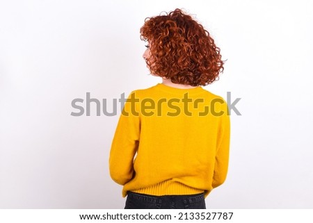 The back view of young redhead girl wearing yellow sweater over white background  Studio Shoot.
