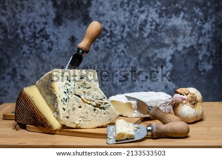 Still life with tacos of delicious and fragrant blue cheeses and brie cheese, a cured Manchego cheese and a head of garlic with small cheese knives and bamboo boards