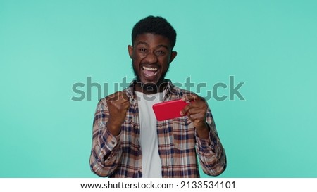 Worried candid addicted african american man enthusiastically playing racing video games on mobile phone. Young guy using smartphone gadget app with drive simulator isolayed on blue studio background Royalty-Free Stock Photo #2133534101