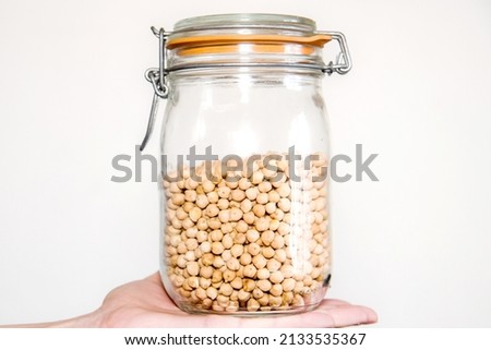 A hand holding a glass jar full of chickpeas. Concept of storage of legumes in the pantry. Vegetal protein. White background. Royalty-Free Stock Photo #2133535367