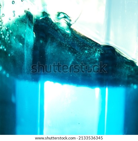 There are the waves and splashes of azure liquid in a glass container that let sunlight through