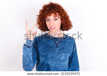 young redhead girl wearing blue sweater over white background smiling and looking friendly, showing number two or second with hand forward, counting down