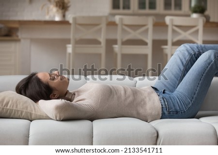 Young peaceful woman fell asleep on sofa at home. Serene female put hands behind head lying on cozy comfort couch in modern living room. Stress-free healthy daytime nap, climate control inside concept Royalty-Free Stock Photo #2133541711