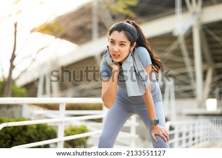 Asian woman wiping sweat on face and neck during exercise in the city at sunrise. Young asian female take a break from training before workout, cardio. Healthy and active lifestyle concept. Royalty-Free Stock Photo #2133551127