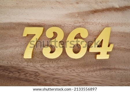 Wooden  numerals 7364 painted in gold on a dark brown and white patterned plank background.
