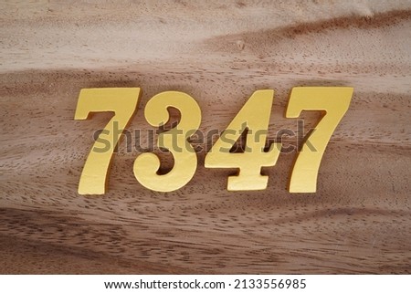Wooden  numerals 7347 painted in gold on a dark brown and white patterned plank background.