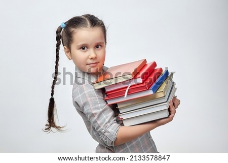 little girl holds a large stack of books in front of her. photo shoot in the studio on a white background.