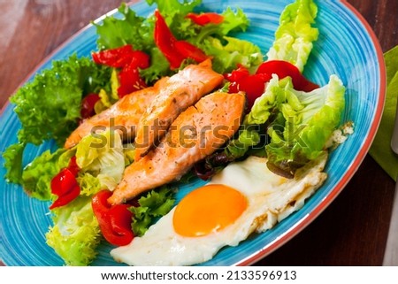 Image of plate with fried trout, egg, vegetables and green lettuce at table