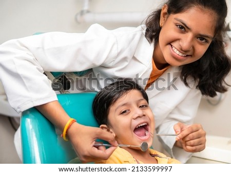 Little boy sitting on the dental chair with open mouth and a female dentist doing his oral checkup at dentist clinic. Royalty-Free Stock Photo #2133599997