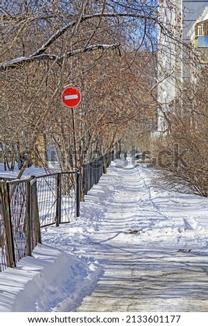 Forbidding road sign near a snow-covered sidewalk on a spring day