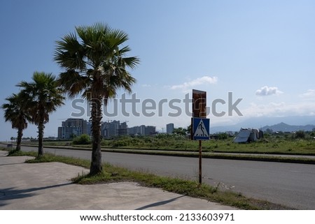 palm trees grow along the side of the highway where there is a sign of the passage and in the distance you can see large city buildings