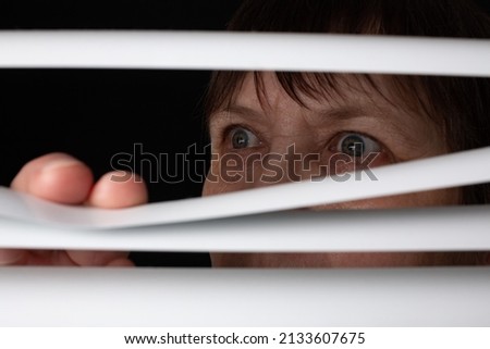 An elderly woman peers through the blinds through the window. Royalty-Free Stock Photo #2133607675