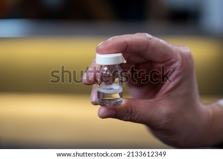Close up of hand holding a vaccine glass bottle with isolated blur background. No label on glass bottle. 
