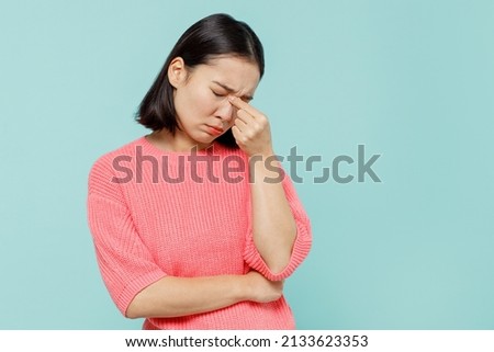 Young pensive sad woman of Asian ethnicity 20s wearing pink sweater keep eyes closed rub put hand on nose isolated on pastel plain light blue color background studio portrait. People lifestyle concept Royalty-Free Stock Photo #2133623353